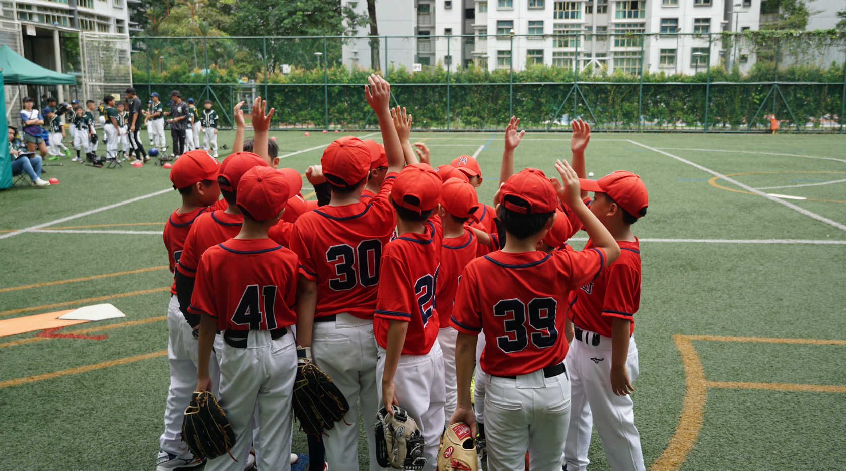 A group of young baseball players raising their hands and cheering together before a game.